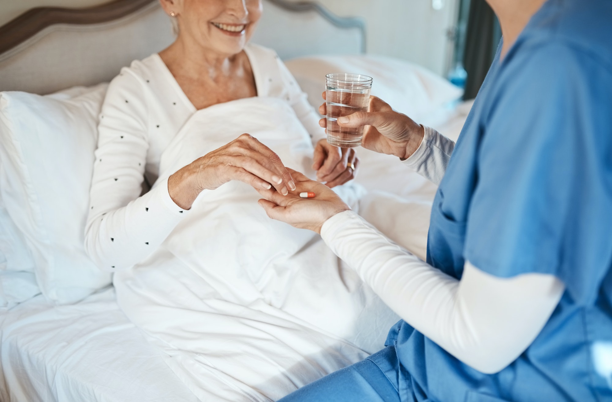 Shot of a nurse giving a senior woman her medication to take with a glass of water in bed